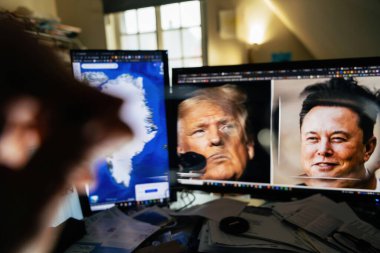 Paris, Fransa - 1 Ocak 2025: Biri Donald Trump ve Elon Musk 'u gösteren, diğeri de Grönland haritasını gösteren, ön planda dağınık bir masa bulunan iki monitöre odaklı gözlük..