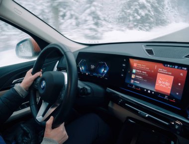 Almanya - 3 Ocak 2025: Bir sürücü, kar yağışlı kış koşullarında saatte 58 km hızla BMW iX1 sürerken Spotify çalma listesini dinliyor,