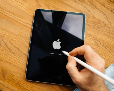 Paris, Fransa - 27 Mart 2019: Başlangıçta Apple logosunu gösteren siyah ekran bir iPad Pro, aşağıdaki ahşap yüzeyde duran bir Apple kalemi tutuyor..