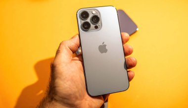 PAris, Fransa - 29 Eylül 2022: Üç kameralı gümüş bir iPhone Pro, canlı sarı bir arka plana karşı, parlak ve modern yapısını vurguluyor..