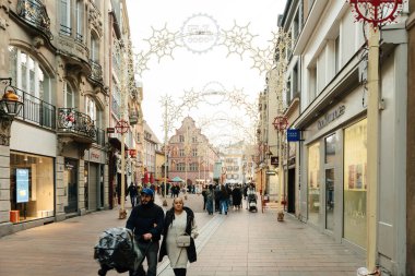 Mulhouse, Fransa - 26 Aralık 2024: Mulhouse, Fransa 'da canlı bir cadde, Noel ışıkları ve şenlikli dekorasyonlarla süslenmiş, insanların geçmişteki dükkanları ve tarihi mimariyi gezdiği.