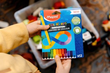Paris, Fransa - 28 Aralık 2024: Maped Color 'Peps ambalajı tutan, canlı renkler ve renkli bir iç mekanda sonsuzluk temalı parlak bir tasarım sunan bir kişi.