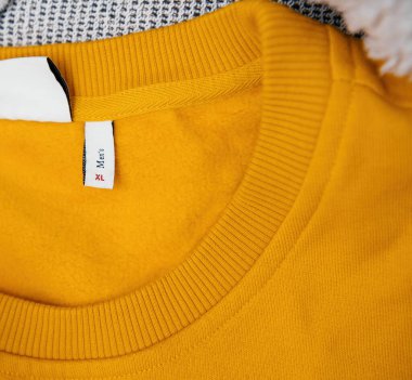 Sarı erkek kazağının yakın plan görüntüsü XL beden etiketini ve kaburgalı yakasını gösteriyor, dokuyu ve kumaşın detaylarını vurguluyor..