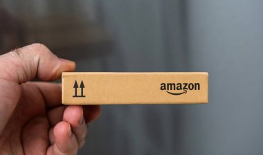 Paris, Fransa - 22 Kasım 2021: Elde tutulan, tarafsız bir arkaplan ile yukarı doğru ok sembolleri gösteren kompakt Amazon damgalı bir karton paket.