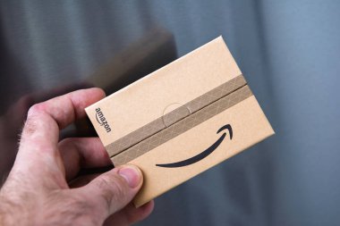 Paris, Fransa - 22 Kasım 2020: Amazon 'un sembolik gülümseme logosuna sahip küçük bir Amazon karton paketi ile parlak metalik arka planda tutulan bir elin yakın çekimi.