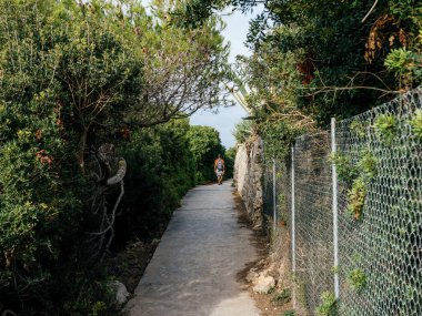 A man walks alone along a scenic path in Mallorca, Spain, carrying a backpack on trail is surrounded by lush greenery and offers picturesque views of the island natural beauty clipart