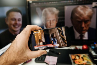 Paris, Fransa - 20 Ocak 2025: Donald Trump 'ın göreve başlama törenini gösteren akıllı telefonu tutan bir el, arka planda Elon Musk' un bulanık portreleri ve resmi Trump fotoğrafları var..