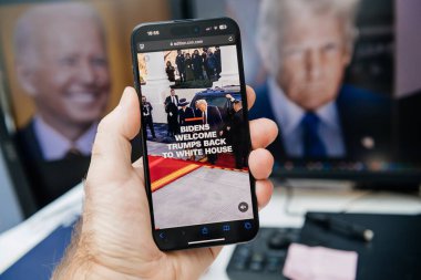 Paris, Fransa - 20 Ocak 2025: Arkaplanda Biden ve Trump 'ın bulanık görüntüleriyle Bidens' in Trump 'ı Beyaz Saray' a geri getirmesini anlatan bir haber başlığını gösteren akıllı telefonu tutan bir el.