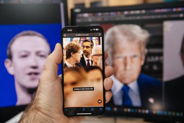 Paris, Fransa - 20 Ocak 2025: Arka planda bulanık Trump ve Zuckerberg portreleriyle Trump 'ın açılış törenine katılan ve aralarında Mark Zuckerberg ve Sundar Pichai' nin de bulunduğu teknoloji liderlerinin de bulunduğu bir CNN makalesinin yer aldığı bir akıllı telefonu tutan bir el.
