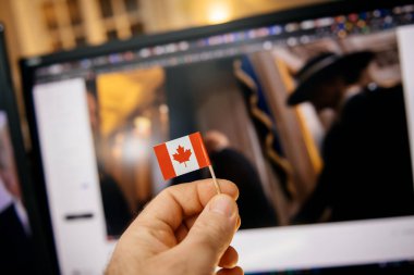 Paris, France - Jan 20, 2025: A hand holding a miniature Canadian flag, with Melania Trump in her iconic hat blurred in the background during Donald Trump s inauguration ceremony. clipart