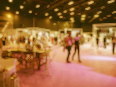 Bir ticaret fuarı etkinliğinin bulanık bir görüntüsü, aydınlatılmış kabinler, katılımcılar, ve canlı ışıklandırmalı geniş bir kapalı mekan.