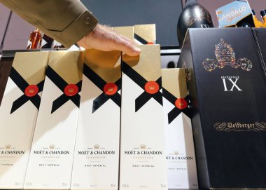 Frankfurt, Almanya - 30 Aralık 2024: Moet ve Chandon Brut Imperial şampanyasının zarif altın ve beyaz kutularda sergilendiği bir raf, bir el seçmesi ile birlikte diğer birinci sınıf içki seçenekleri.