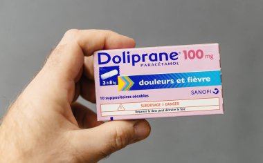 Paris, Fransa - 18 Ocak 2025: Bir el, 3-8 kg ağırlığındaki çocuklar için hedeflenmiş bir kutu Doliprane 100 mg. Ağrı ve ateş düşürücü olarak nitelendirilen kutu, karaciğer hasarı nedeniyle aşırı doz almamaya karşı uyarıda bulunuyor..