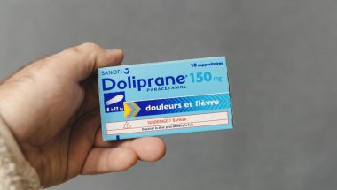 Paris, France - Jan 18, 2025: A hand holding a box of Doliprane 150mg suppositories, containing paracetamol for pain and fever relief, designed for children weighing 8 to 12 kg. clipart