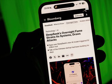 Paris, Fransa - 28 Ocak 2025: Bloomberg 'in DeepSeek' in sistemlerini zorlayan ani şöhreti ve yeşil ışıklı arka plana siber saldırılar düzenlemesi hakkındaki makalesini gösteren akıllı telefon ekranı, dramatik bağlamı vurguluyor.