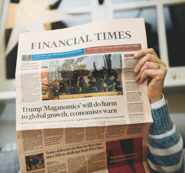 Paris, France - Jan 10, 2025: A woman reading the Financial Times featuring headlines about Trump's Maga-nomics, potential global economic harm, and Tesla's delivery decline. clipart