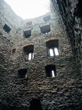 Terk edilmiş bir kalenin taş duvarları, bulutlu bir gökyüzünün altında birden fazla kemerli penceresi olan, rahatsız edici derecede gizemli ve ıssız bir titreşim yayan..