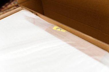 İçi beyaz koruyucu köpükle kaplı karton bir kutunun yakın çekimi ve ince şeffaf bir tabakayla kısmen kaplanmış sarı bir etiket..