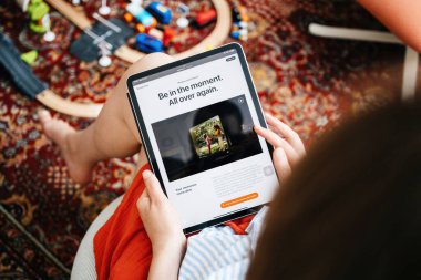 Paris, Fransa - 11 Haziran 2023: Apple Vision Pro ile ilgili bir tablet tutan ve okuyan bir kişi, ekranda oyuncak tren setiyle ilgili bir makale ile arka planda desenli bir halının üzerinde görünür..