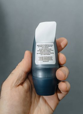 Paris, France - Feb 13, 2025: A person holds a Dove roll-on deodorant bottle with an open label revealing instructions and warnings in multiple languages against a neutral gray background. clipart