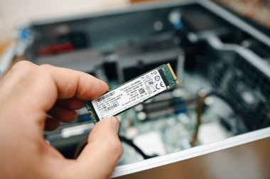 Frankfurt, Almanya - 15 Haziran 2023: AA üyesi güçlü bir çalışma istasyonunu yükseltirken bir SK Hynix NVMe SSD tutuyor. Arka plandaki açık bilgisayar dosyası kurulum için iç bileşenleri ortaya çıkarır.