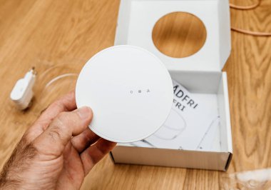Paris, Fransa - 17 Haziran 2021: Bir kişi beyaz IKEA TRADFRI akıllı merkezini ahşap bir yüzey üzerinde, etrafına saçılmış bir güç adaptörü, manuel ve plastik ambalajla açık ambalajının üzerinde tutar..