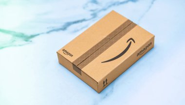 Paris, Fransa - 22 Kasım 2022: Pürüzsüz, açık renkli bir yüzeye küçük bir Amazon paketi yerleştiriliyor, tanınabilir Amazon logosu ve ambalaj tasarımı bir ok sembolü ile sergileniyor.