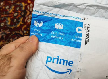 Paris, Fransa - 12 Aralık 2022: Bir kişi Hermes nakliye etiketli Amazon Prime yastıklı bir zarf tutuyor, mavi tanıtım simgeleri içeriyor..