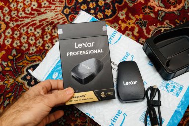 Paris, Fransa - 12 Aralık 2022: Bir kişi Amazon Prime ambalajından Lexar Profesyonel CFexpress kart okuyucusunu açıyor, siyah ambalaj, cihaz, USB-C kablo ve plastik tepsiyi desenli bir halı üzerinde sergiliyor.