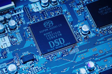 Paris, France - Mar 29, 2023: A close-up view of a Sony Super Audio CD player circuit board features a DSD chipset with intricate electronic components, capacitors, and traces on a blue PCB. clipart