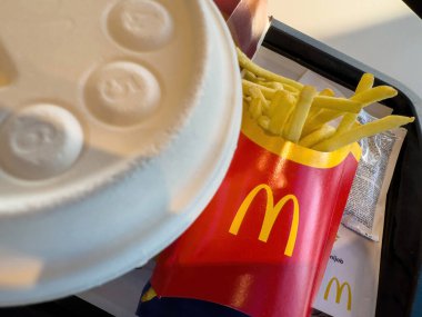 Berlin, Almanya - 29 Sep 2023: McDonald 's fast food tepsisi, kırmızı patates kızartması kabını altın kızartmalarla, markalı içecek bardağı kapağını ve yumuşak iç aydınlatma altında görünen kağıt parçalarını gösteriyor.