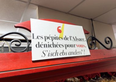 Paris, Fransa - 12 Aralık 2025: Alsace 'nin bölgesel özelliklerini Fransız ve Alsas dillerinin eğlenceli bir karışımıyla sergileyen bir dükkana imza atın. Tabela yerel bulgular için sıcak ve davetkar bir ton sunuyor