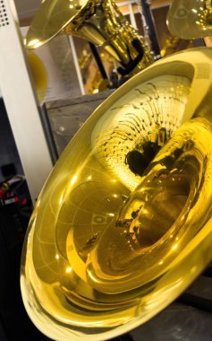 İyi ışıklandırılmış bir müzik dükkanındaki tavan kiremitlerini ve ışıkları yansıtan parlak, pirinçten bir çanın yakın görüntüsü sergilenmekte olan çeşitli altın pirinç enstrümanlarla dolu.