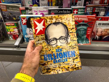 Frankfurt, Almanya - 13 Mart 2025: Friedrich Merz 'in yer aldığı derginin Mart 2025 tarihli sayısını elinde tutan kişi, kapağında Der Millionen-Tanzler başlığıyla bir gazete bayisinde altın sikkelerle çevrili.