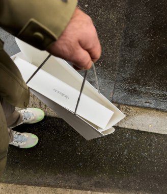Paris, Fransa - 13 Mart 2025: Islak bir şehir kaldırımında gündelik kıyafetlerle yürürken içinde MacBook Air M4 baskının bulunduğu beyaz bir Apple Store kağıt çanta taşıyan bir kişinin yakın çekim görüntüsü