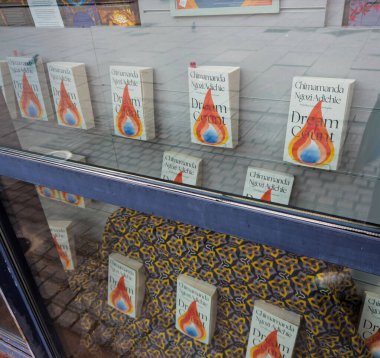 Paris, Fransa - 13 Mart 2025: Chimamanda Ngozi Adichies Rüya Sayısının birden fazla kopyası cam raflarda ve sokak yansımaları olan desenli kumaş sergisi