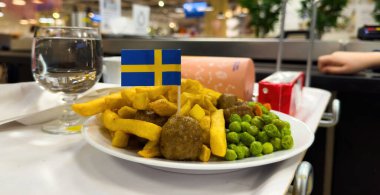 Paris, Fransa - 15 Mart 2025: IKEA restoranında küçük bir İsveç bayrağıyla süslenmiş ve bir bardak su ve meyve suyu kartonunun yanına yerleştirilmiş, patates kızartması ve yeşil bezelyeli İsveç köftesi servis ediliyor
