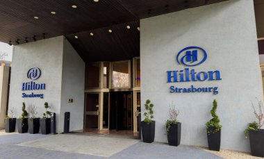 Strasbourg, Fransa - 26 Mar 2025: Hilton Strasbourg Oteli 'nin ana girişi modern açık gri cepheli, siyah ekiciler ve lüks bir ortamda dönen kapılar.