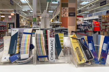 Paris, Fransa - 27 Mart 2025: Çeşitli boya markalarından alınmış renkli kitapçıklar, arka planda koridorları ve tabelaları olan bir Fransız DIY mağazasındaki tezgahın üzerinde açık akrilik tutucular halinde düzenlenmiştir.