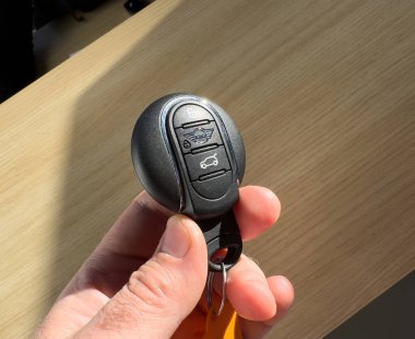Paris, Fransa - 27 Mart 2025: Bir el, MINI 'nin birleşik kilidi, kilidi, kilidi ve bagaj düğmeleri olan ve MINI logosunun yer aldığı bir MINI anahtarlığını bir bayiliğin içinde, günışığıyla aydınlanmış tahıl yüzeyine karşı koyan bir el tutuyor.