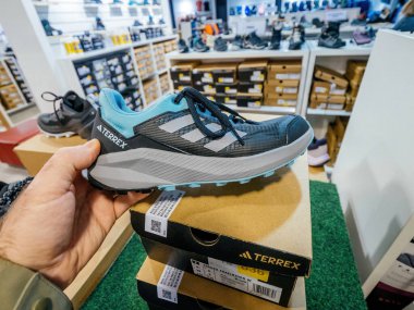 Freiburg, Almanya - 10 Şubat 2025: Adidas tarafından çalıştırılan bir Terrex yolu, arka planda ayakkabı ve ürün paketleriyle dolu raflarla dolu bir mağaza koridorundaki ayakkabı kutularının üzerinde tutuluyor.