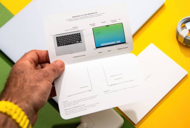 Paris, Fransa - Mar 13, 2025: Katlanmış MacBook Air 'in el ele tutuşması bakış açısı hızla klavye ve ekran diyagramını renkli bir masaüstünde boks yaparken etiketlenmiş portların yanında göstermeye başlayın