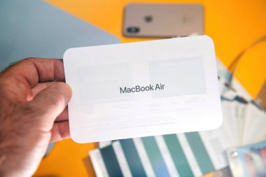 Paris, Fransa - 13 Mart 2025: Basılı bir MacBook Air M4 başlangıç belgesi, telefon, kablo, renk örnekleri ve aksesuarlarla dağılmış yaratıcı bir masanın üzerindeki boks süreci sırasında elde tutuldu
