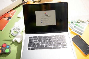 Paris, Fransa - 13 Mar 2025: MacBook Air M4, Apple Intelligence kurulum ekranının açılışı sırasında şarj aleti, kablo, telefon, dergi ve renk örneklerinin yer aldığı yaratıcı bir masa ortamı sundu