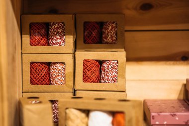 Renkli sicim topları pencereli karton kutularda paketlenir, ahşap bir rafta el işi ve dekorasyon için sergilenir..