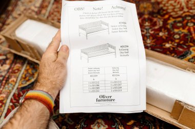 Paris, Fransa - 25 Ekim 2022: Elinizde Oliver Mobilya için bir montaj kılavuzu var, çeşitli gündüz yatakları için hazırlanan düzeneği halı üzerindeki paketsiz bir kutunun arka planına karşı ayrıntılı olarak anlatıyor..