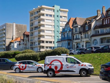 Le Touquet, Fransa - 23 Ağustos 2023: Fransa 'da Le Touquet, Fransa' da bir caddeye park edilmiş Veolia markalı araçlar, arka planda modern dairelerden geleneksel evlere zıt mimari tarzlara sahip.
