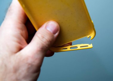 Paris, Fransa - 10 Mart 2025: Zarar görmüş sarı plastik bir iPhone çantası, şarj portu açıklığının yanında kırık kenarlı, yumuşak mavi arka planda yakın plan gösteriliyor