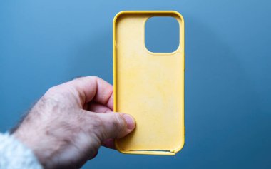 Paris, Fransa - 10 Mart 2025: Bir el, kırık alt kenarı ve büyük kamerayı mavi bir arkaplan üzerinde gösteren, ön cepheden görülen hasarlı sarı plastik bir iPhone kılıfını tutuyor