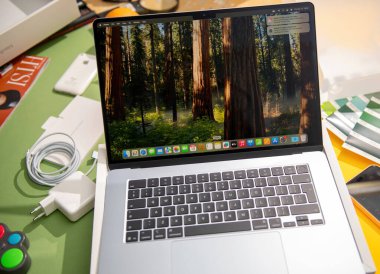 Paris, Fransa - 13 Mar 2025: Yeni açılmış bir MacBook Air M4 dizüstü bilgisayar, renkli bir çalışma alanındaki aksesuarlar ve canlı nesnelerle çevrili bir orman duvar kağıdı sergilenmektedir.